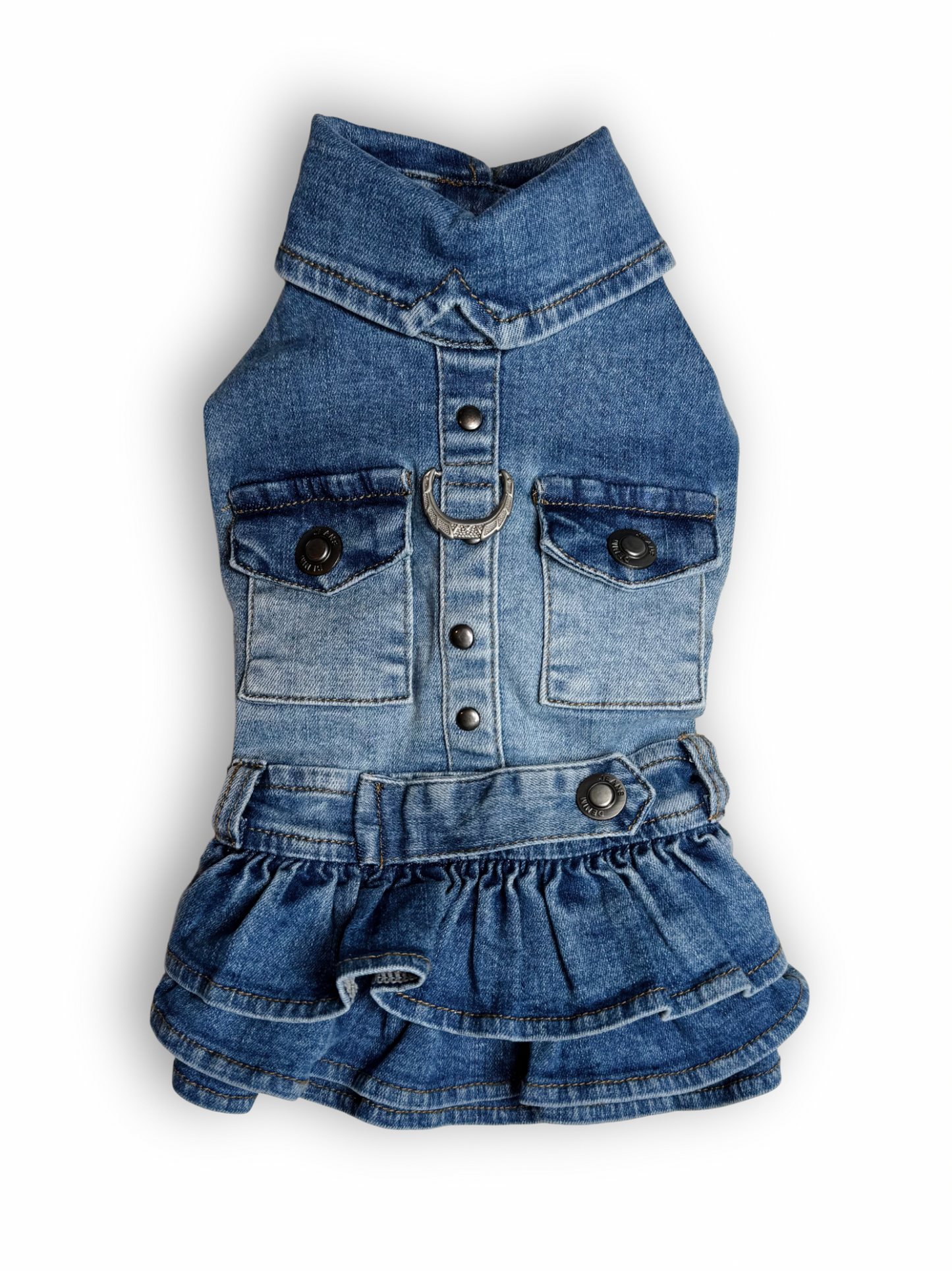A blue denim dog dress with a ruffled layered skirt, collar neck, and sleeveless design. It includes two non-functional pockets and a D-ring for leash attachment.