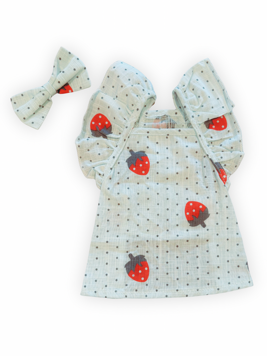 Small dog wearing strawberry and polka dot print dress with ruffle sleeves and matching bow