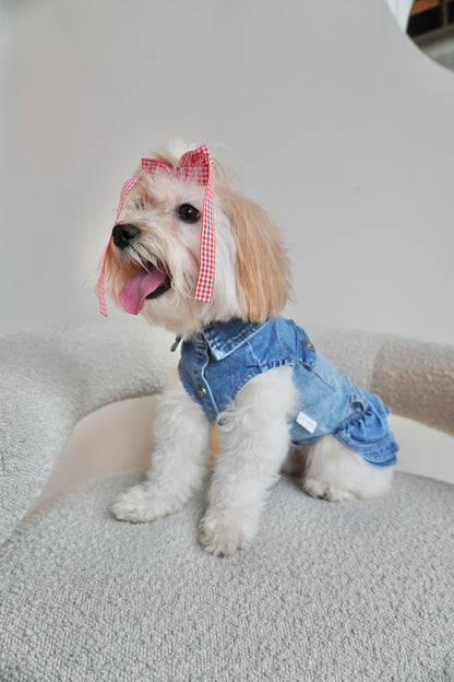 Small dog sitting on boucle chair, wearing a stretchy denim dog dress with front button closure, chest pockets, and a ruffled skirt. Side angle view.